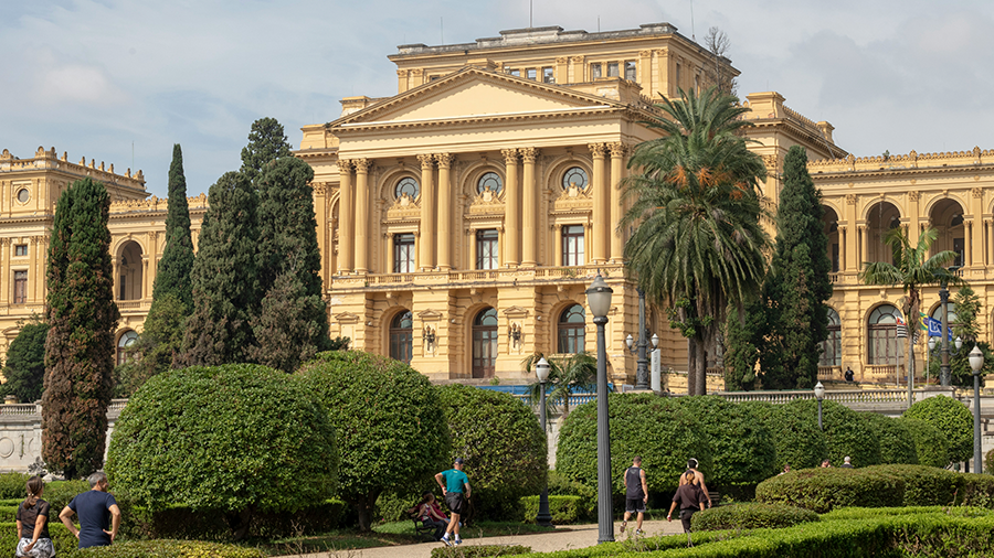 Museu do Ipiranga do lado externo com árvores ao redor e pessoas caminhando