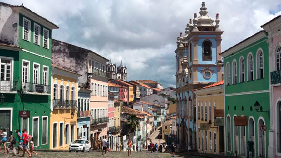 Rua de paralelepípedo do Pelourinho, com diversas casas coloridas e algumas pessoas caminhando