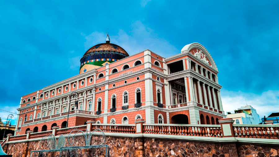 Área externa do Teatro Amazonas, onde é possível ver a enorme cúpula, composta por 36 mil peças nas cores da bandeira brasileira e o céu azul ao fundo