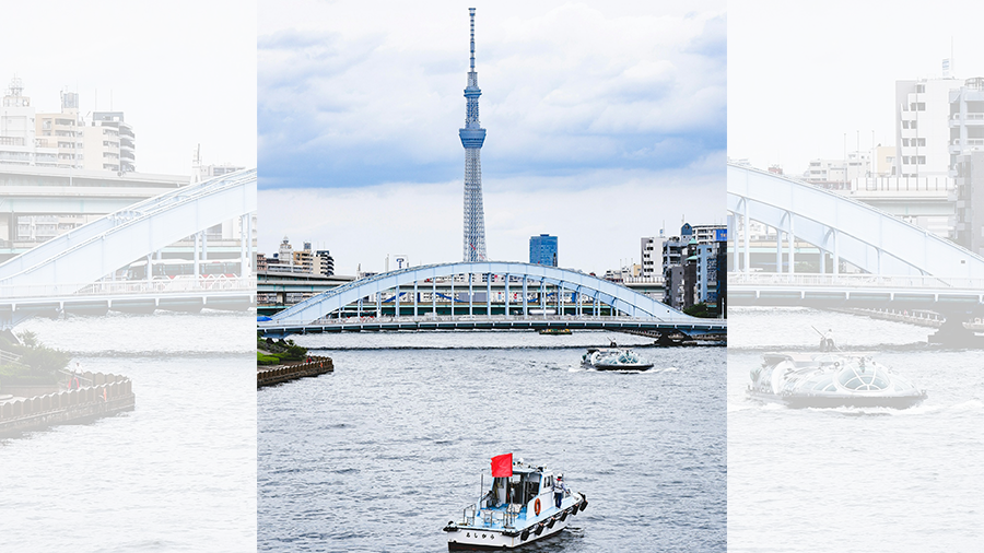 Imagem diurna da torre Skytree ao fundo, com uma arquitetura japonesa, um rio à frente com alguns barcos e outras construções ao redor.